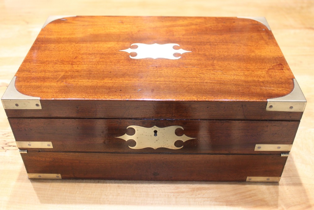 A closed rectangular late Georgian mahogany campaign writing slope featuring flush brass corner brackets, protective straps, and a decorative brass keyhole escutcheon.