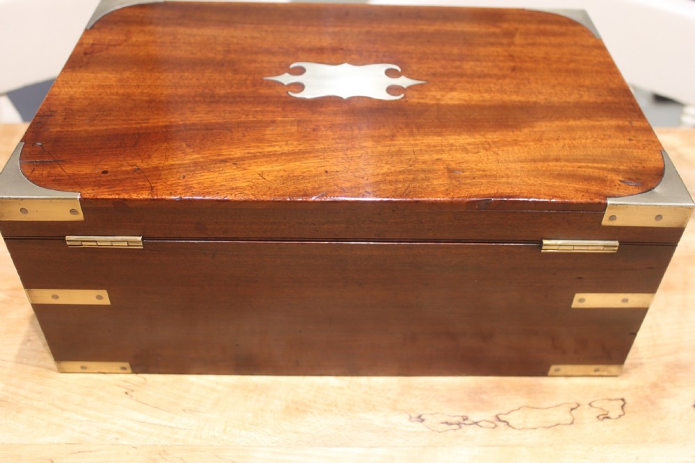 A closed rectangular late Georgian mahogany campaign writing slope featuring flush brass corner brackets, protective straps, and a decorative brass keyhole escutcheon. View IV