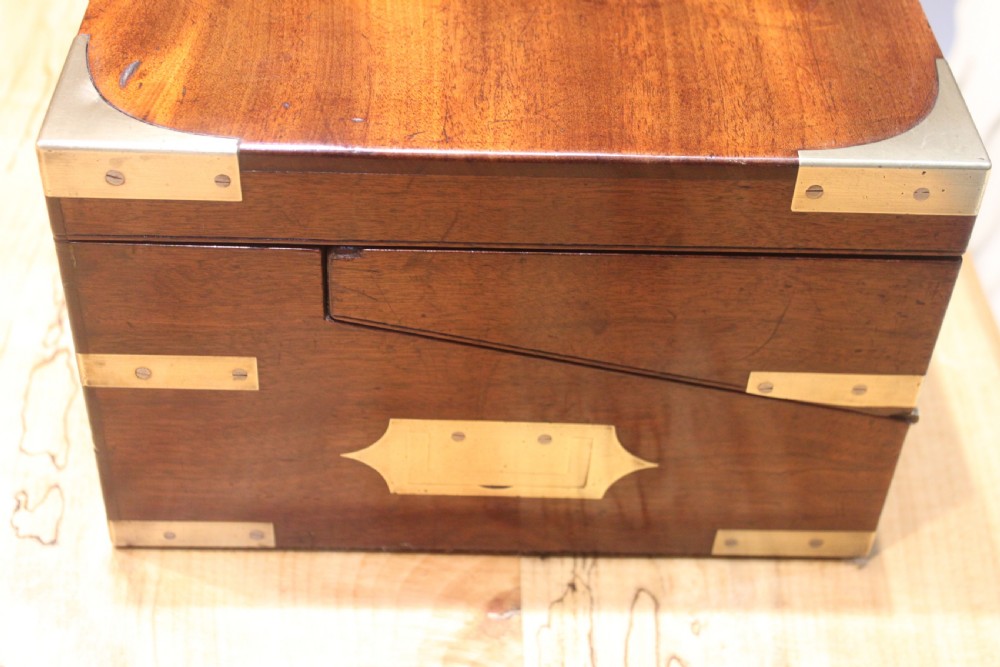 A closed rectangular late Georgian mahogany campaign writing slope featuring flush brass corner brackets, protective straps, and a decorative brass keyhole escutcheon. View V