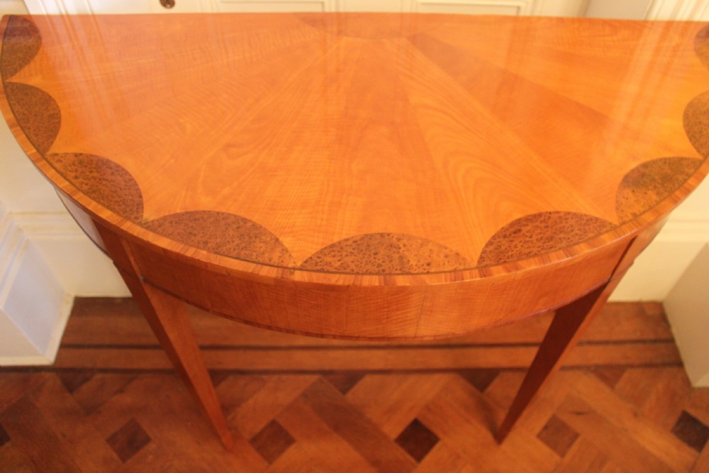 An early 19th-century semi-circular satinwood demi-lune console table featuring decorative top marquetry and four square tapered legs. View II