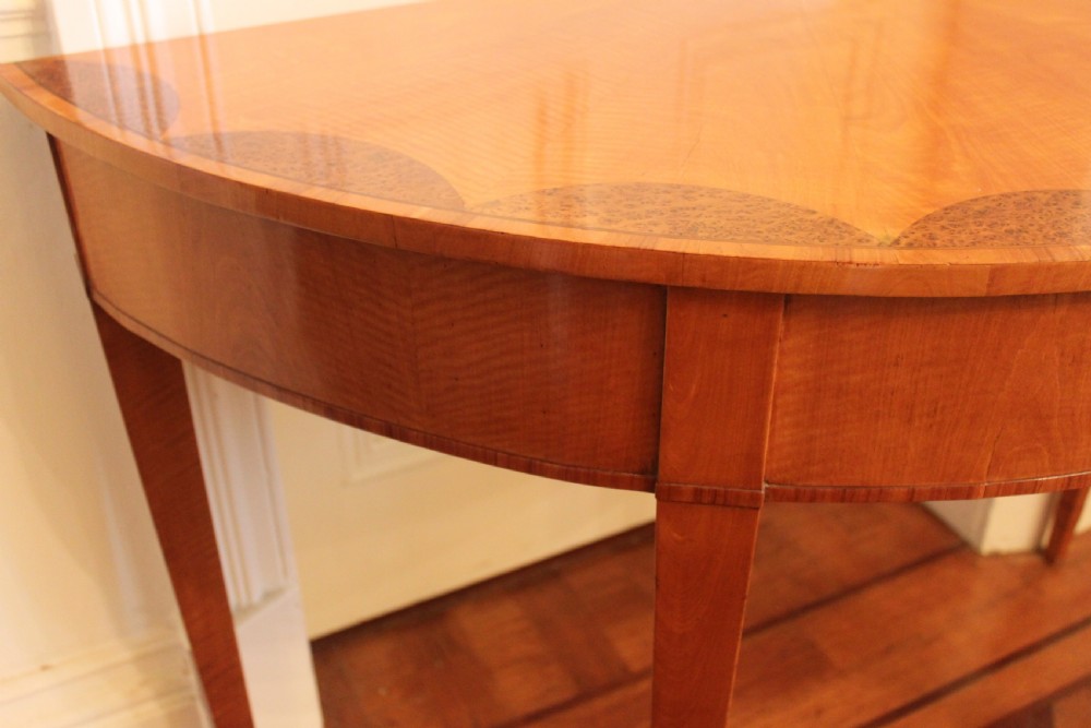An early 19th-century semi-circular satinwood demi-lune console table featuring decorative top marquetry and four square tapered legs. View V