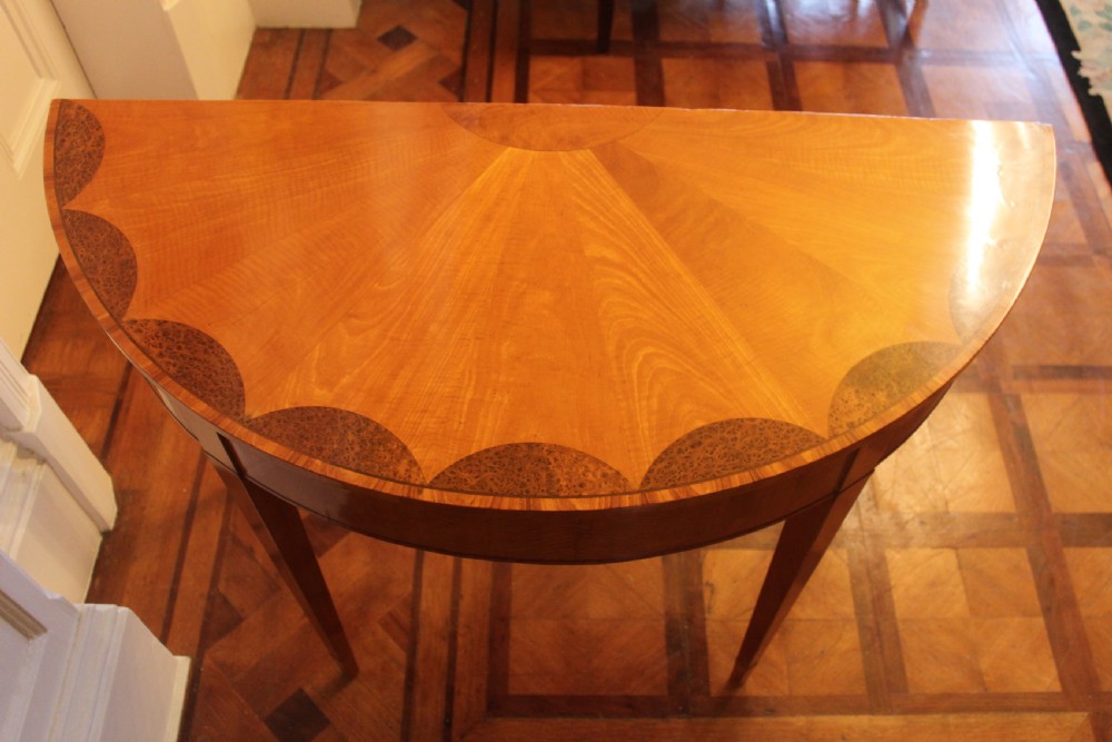 An early 19th-century semi-circular satinwood demi-lune console table featuring decorative top marquetry and four square tapered legs. View X