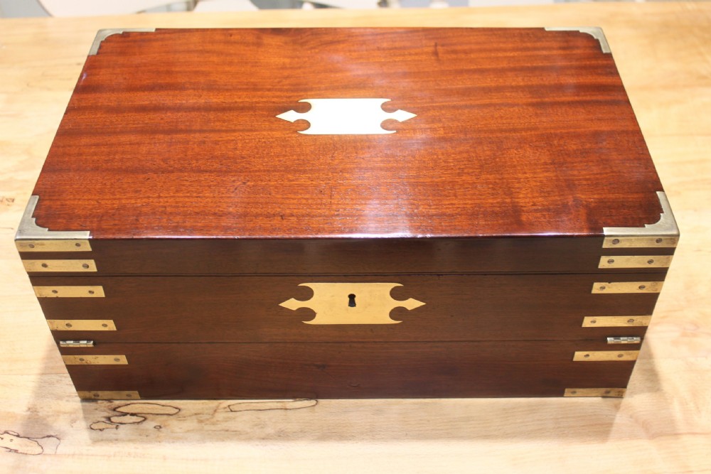 A 19th-century rectangular mahogany campaign writing slope with flush brass corner brackets, brass side strapping, an inlaid brass keyhole escutcheon, and a central brass plaque on the lid.
