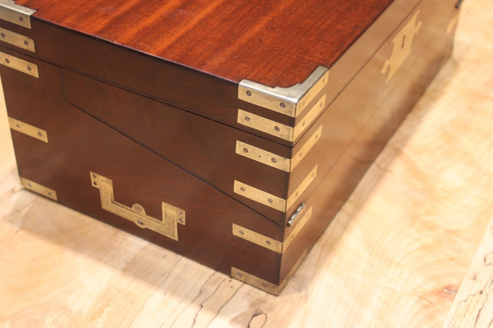 A 19th-century rectangular mahogany campaign writing slope with flush brass corner brackets, brass side strapping, an inlaid brass keyhole escutcheon, and a central brass plaque on the lid. View VI