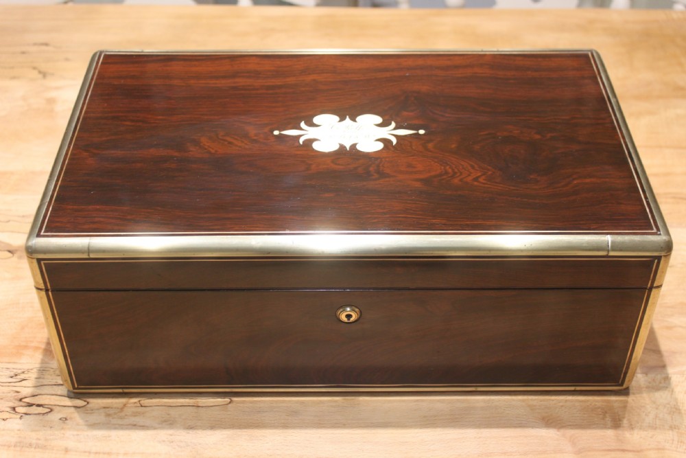 A closed rectangular dark rosewood writing slope featuring brass-bound corners, fine brass line inlay, a brass keyhole escutcheon, and an engraved central brass cartouche.