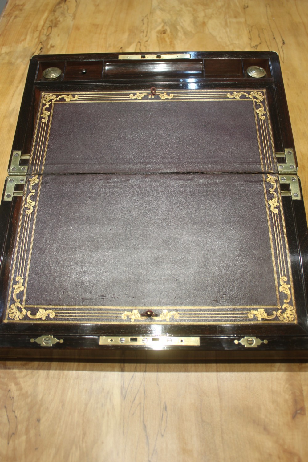 A closed rectangular dark rosewood writing slope featuring brass-bound corners, fine brass line inlay, a brass keyhole escutcheon, and an engraved central brass cartouche. View VI