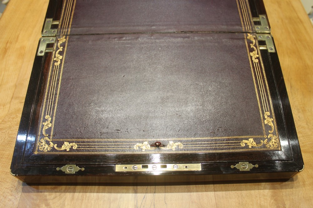 A closed rectangular dark rosewood writing slope featuring brass-bound corners, fine brass line inlay, a brass keyhole escutcheon, and an engraved central brass cartouche. View VII