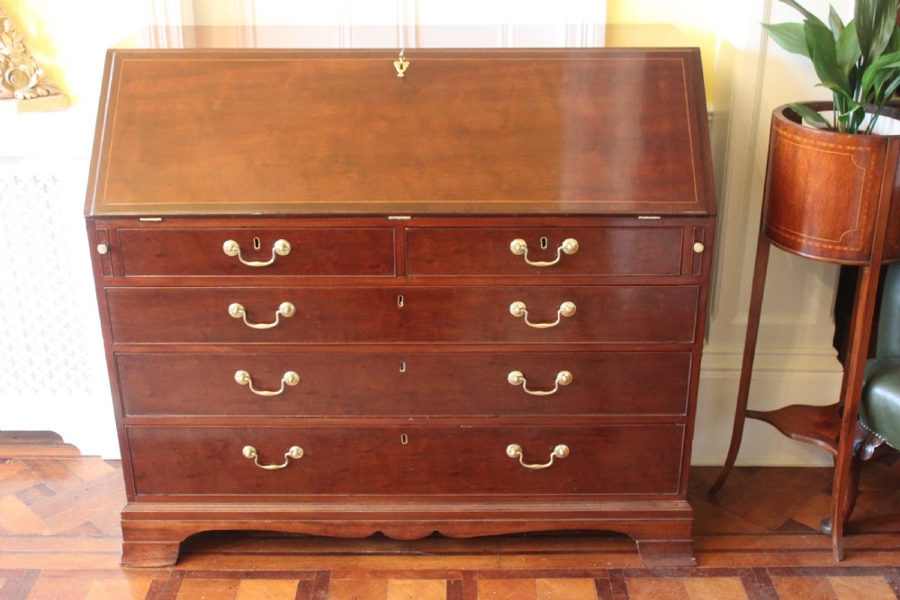 An 18th-century George III mahogany slant-front bureau featuring brass swan-neck handles and inlaid stringing over four graduated drawers.