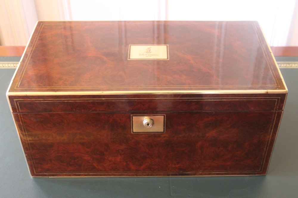 A rectangular Victorian burr walnut writing slope box featuring swirl veneer patterns, brass stringing inlay, a central engraved brass plaque, and a front keyhole escutcheon.