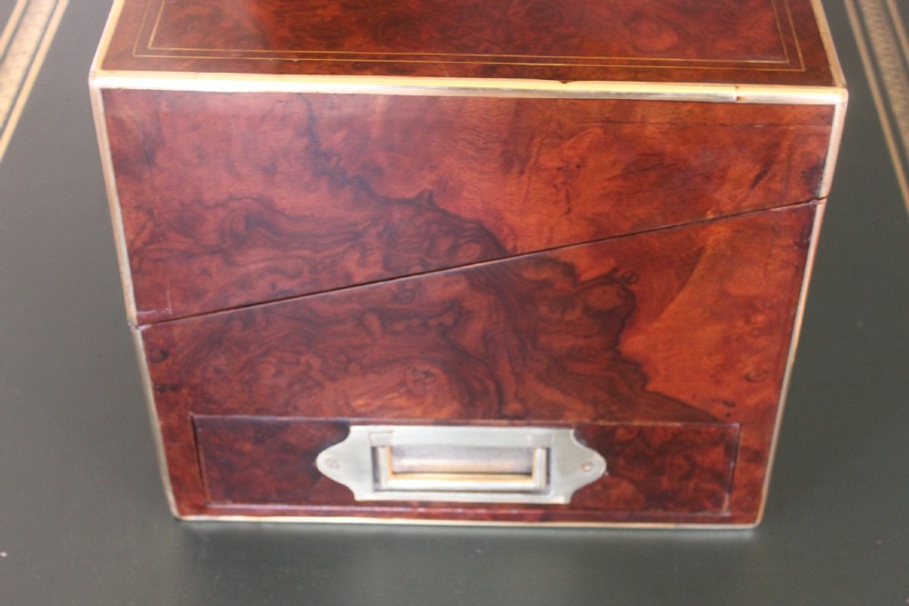 A rectangular Victorian burr walnut writing slope box featuring swirl veneer patterns, brass stringing inlay, a central engraved brass plaque, and a front keyhole escutcheon. View IV