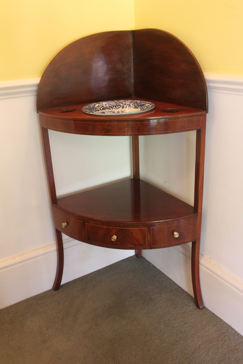 A Georgian mahogany corner washstand featuring an upper arched splashback, a central tier with a drawer, brass knobs, and curved splayed legs. View II