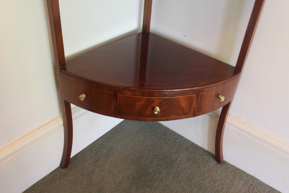 A Georgian mahogany corner washstand featuring an upper arched splashback, a central tier with a drawer, brass knobs, and curved splayed legs. View V