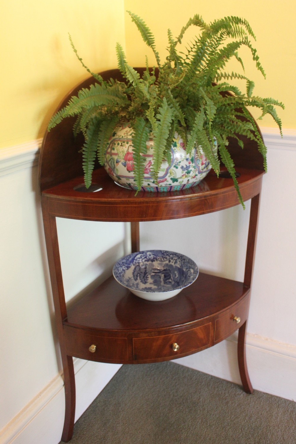 A Georgian mahogany corner washstand featuring an upper arched splashback, a central tier with a drawer, brass knobs, and curved splayed legs. View VII