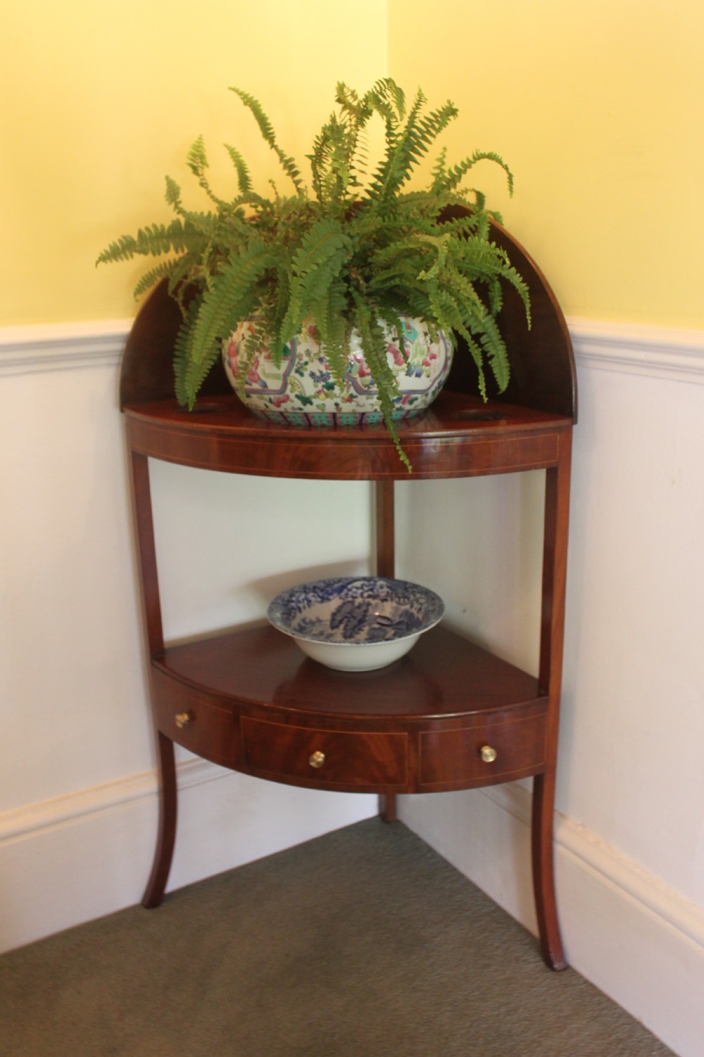 A Georgian mahogany corner washstand featuring an upper arched splashback, a central tier with a drawer, brass knobs, and curved splayed legs. View VIII