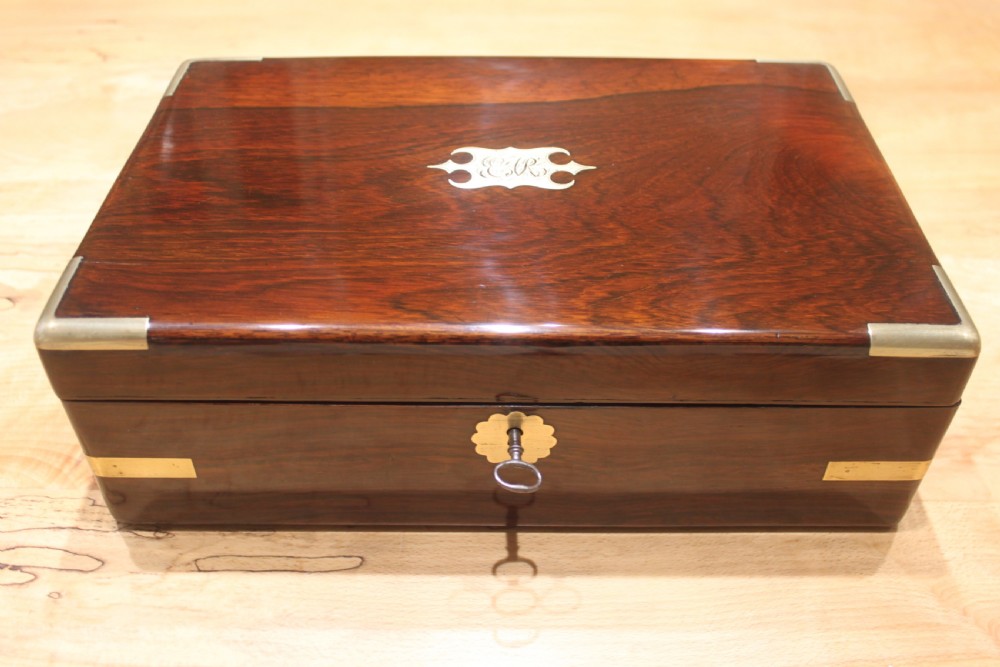 A rectangular Victorian rosewood writing box featuring flush brass corner brackets, a central engraved brass cartouche, and a key inserted into the front keyhole. View II
