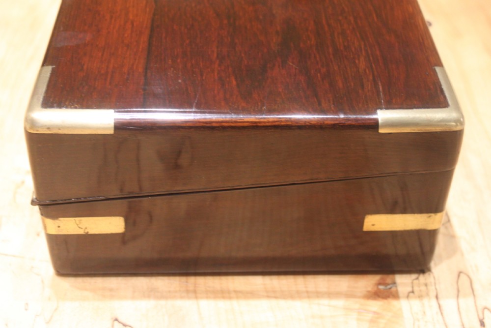 A rectangular Victorian rosewood writing box featuring flush brass corner brackets, a central engraved brass cartouche, and a key inserted into the front keyhole. View III