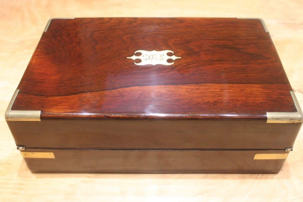 A rectangular Victorian rosewood writing box featuring flush brass corner brackets, a central engraved brass cartouche, and a key inserted into the front keyhole. View IV