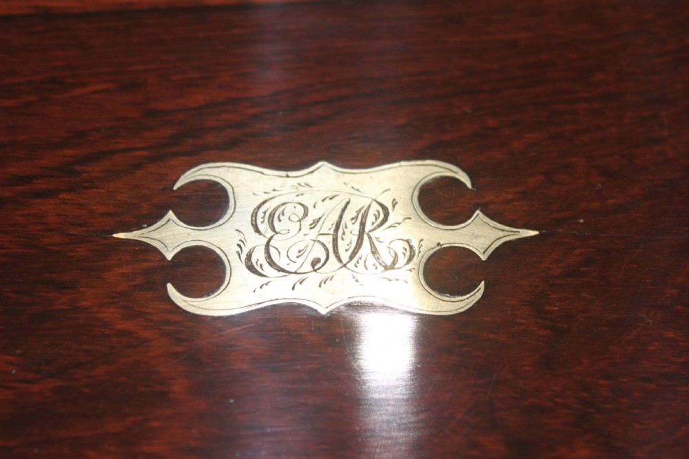 A rectangular Victorian rosewood writing box featuring flush brass corner brackets, a central engraved brass cartouche, and a key inserted into the front keyhole. View VI
