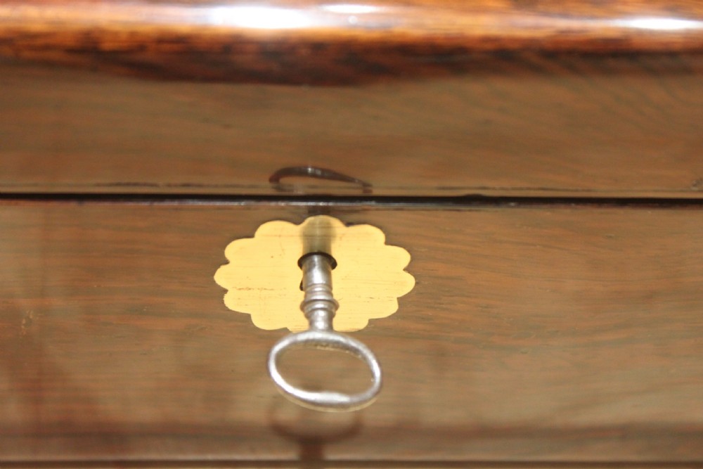 A rectangular Victorian rosewood writing box featuring flush brass corner brackets, a central engraved brass cartouche, and a key inserted into the front keyhole. View VII