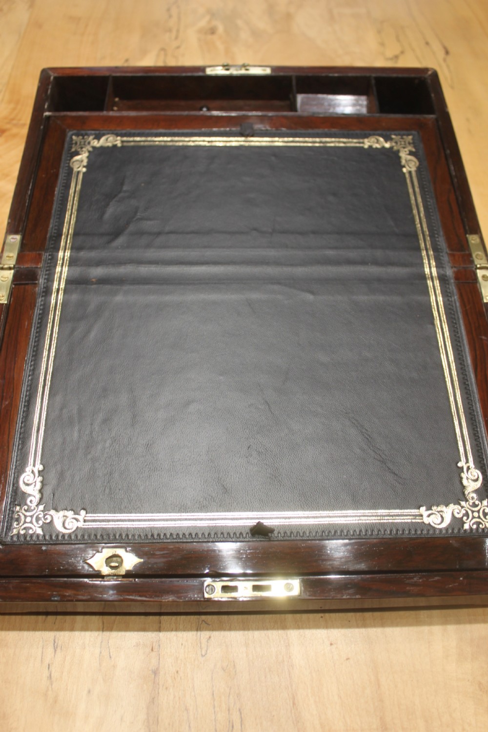 A rectangular Victorian rosewood writing box featuring flush brass corner brackets, a central engraved brass cartouche, and a key inserted into the front keyhole. View VIII