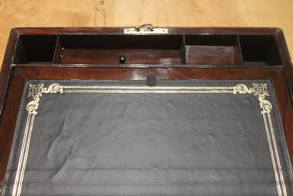 A rectangular Victorian rosewood writing box featuring flush brass corner brackets, a central engraved brass cartouche, and a key inserted into the front keyhole. View IX