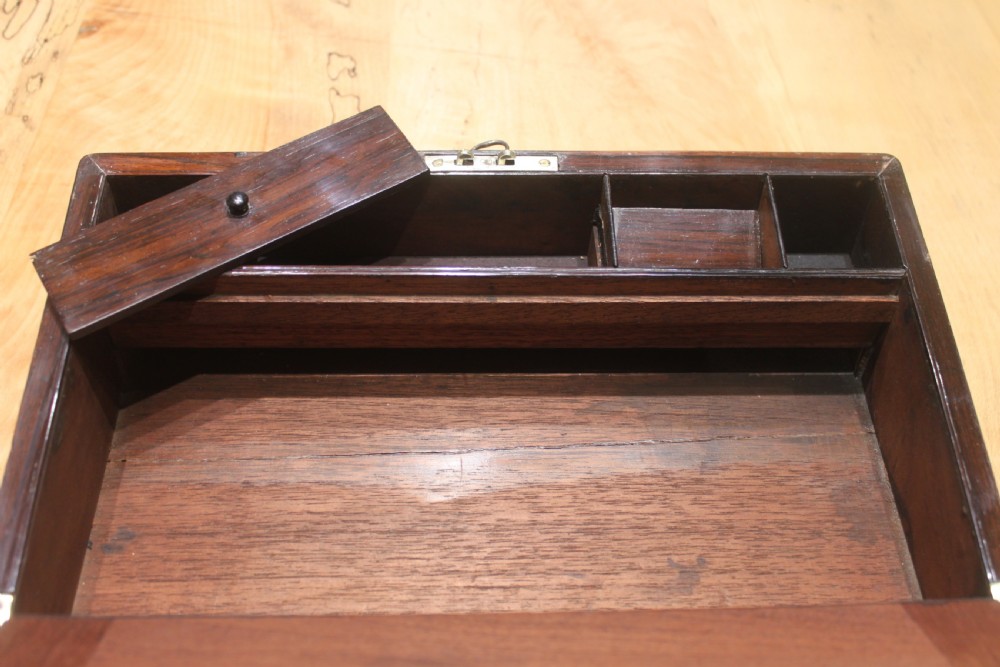 A rectangular Victorian rosewood writing box featuring flush brass corner brackets, a central engraved brass cartouche, and a key inserted into the front keyhole. View XI