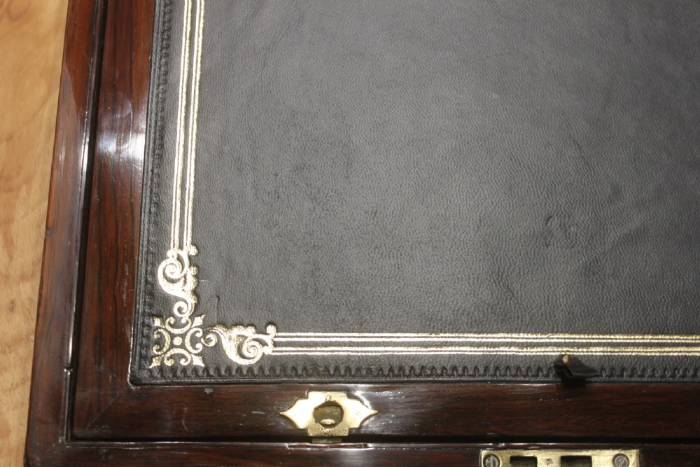 A rectangular Victorian rosewood writing box featuring flush brass corner brackets, a central engraved brass cartouche, and a key inserted into the front keyhole. View XIII