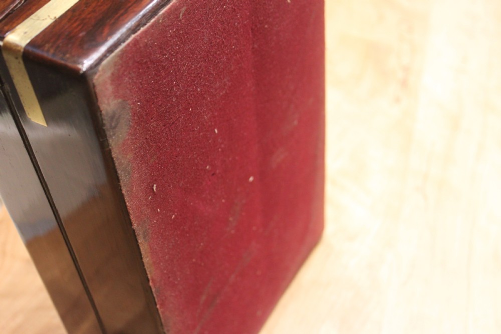 A rectangular Victorian rosewood writing box featuring flush brass corner brackets, a central engraved brass cartouche, and a key inserted into the front keyhole. View XIV