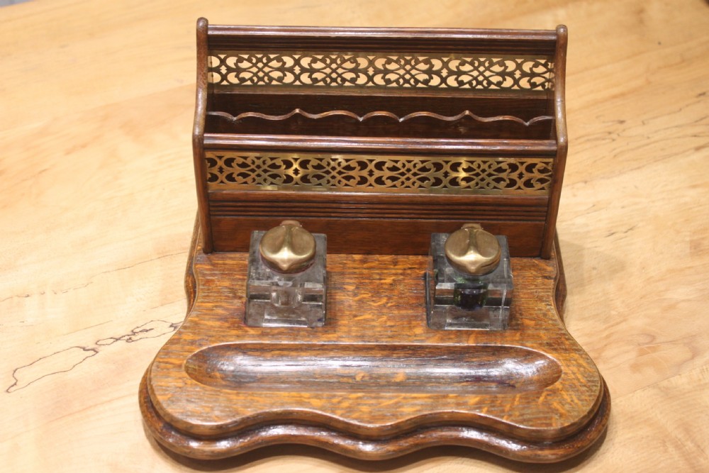 Late Victorian oak standish featuring a stationary gallery with pierced brass trim, two square glass inkwells with brass lids, and a carved pen groove.