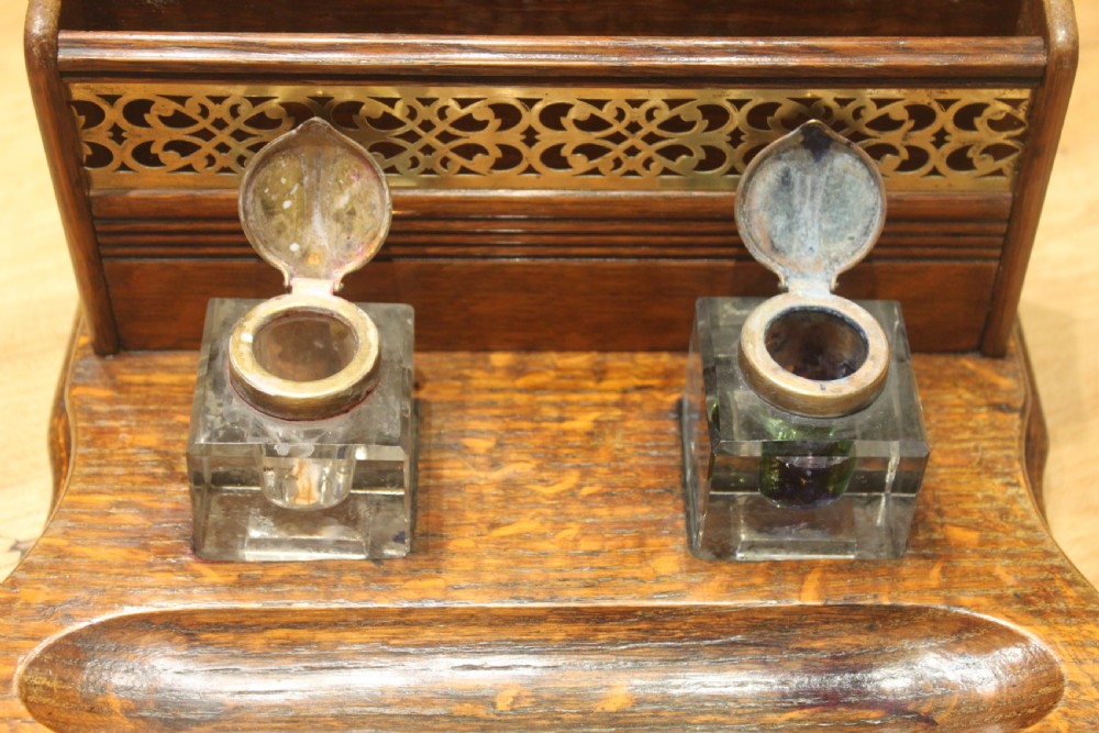 Late Victorian oak standish featuring a stationary gallery with pierced brass trim, two square glass inkwells with brass lids, and a carved pen groove. View III
