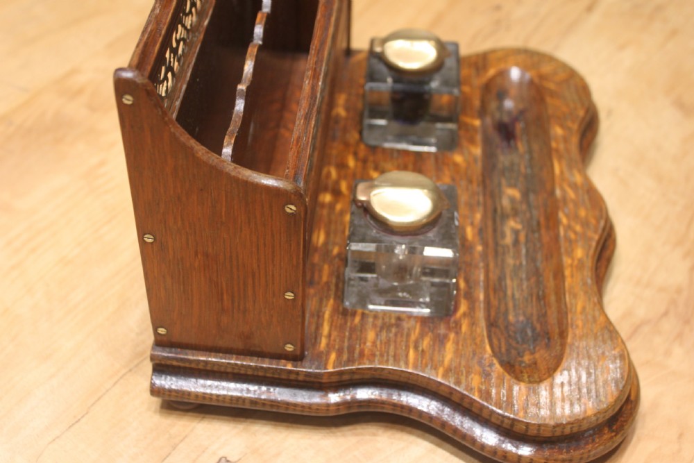 Late Victorian oak standish featuring a stationary gallery with pierced brass trim, two square glass inkwells with brass lids, and a carved pen groove. View V