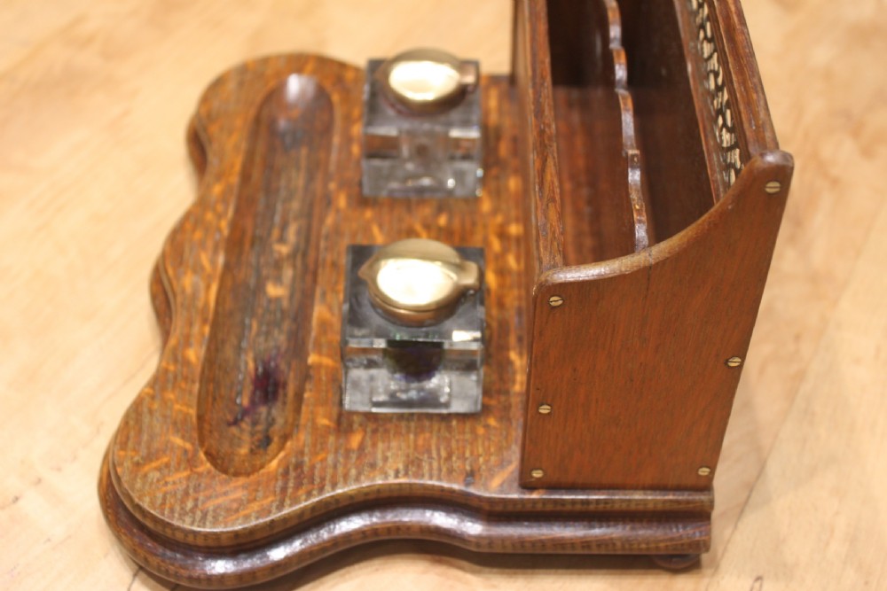 Late Victorian oak standish featuring a stationary gallery with pierced brass trim, two square glass inkwells with brass lids, and a carved pen groove. View VII