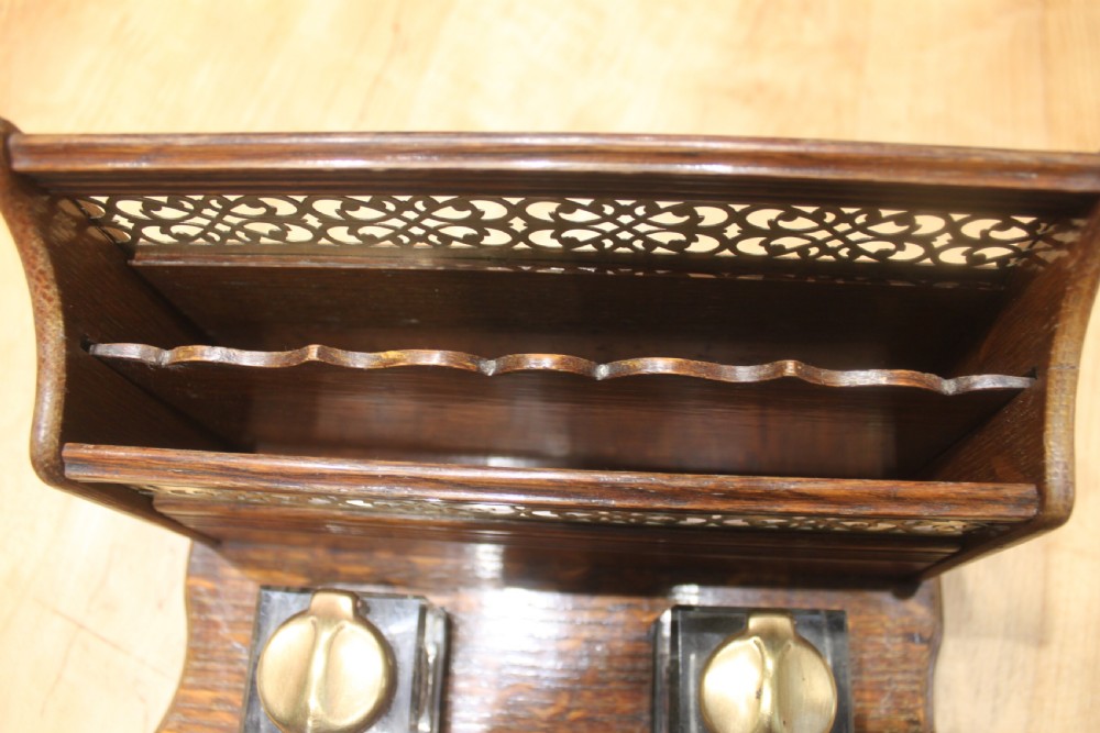 Late Victorian oak standish featuring a stationary gallery with pierced brass trim, two square glass inkwells with brass lids, and a carved pen groove. View IX