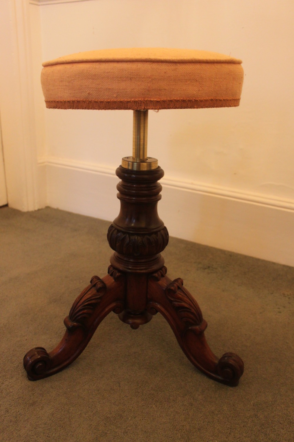 A Victorian mahogany revolving piano stool featuring a circular beige upholstered seat, a turned pedestal with acanthus leaf carving, and tripod scroll feet. View II