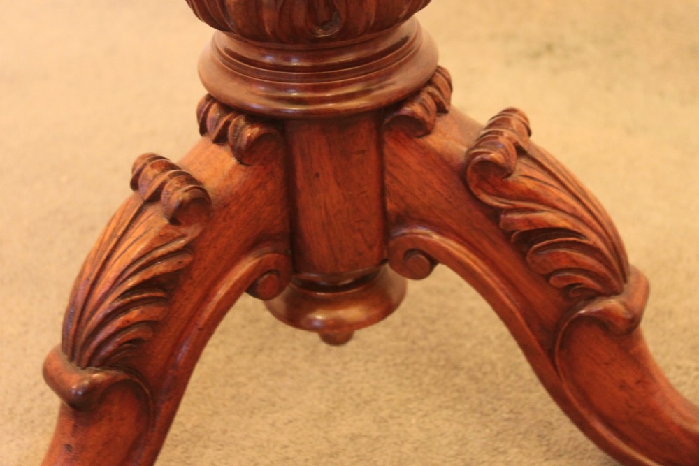 A Victorian mahogany revolving piano stool featuring a circular beige upholstered seat, a turned pedestal with acanthus leaf carving, and tripod scroll feet. View III