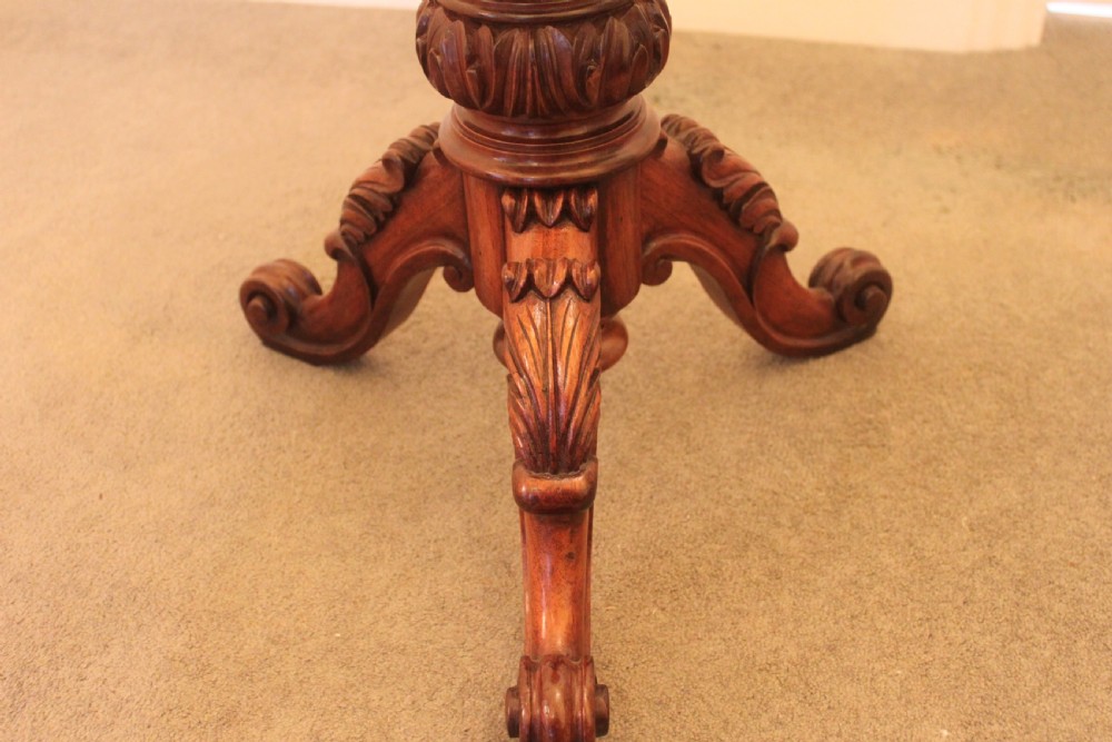 A Victorian mahogany revolving piano stool featuring a circular beige upholstered seat, a turned pedestal with acanthus leaf carving, and tripod scroll feet. View V
