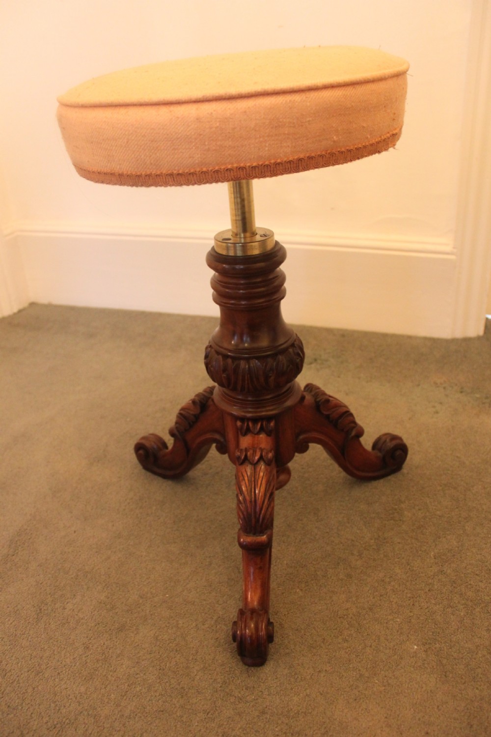 A Victorian mahogany revolving piano stool featuring a circular beige upholstered seat, a turned pedestal with acanthus leaf carving, and tripod scroll feet. View VI