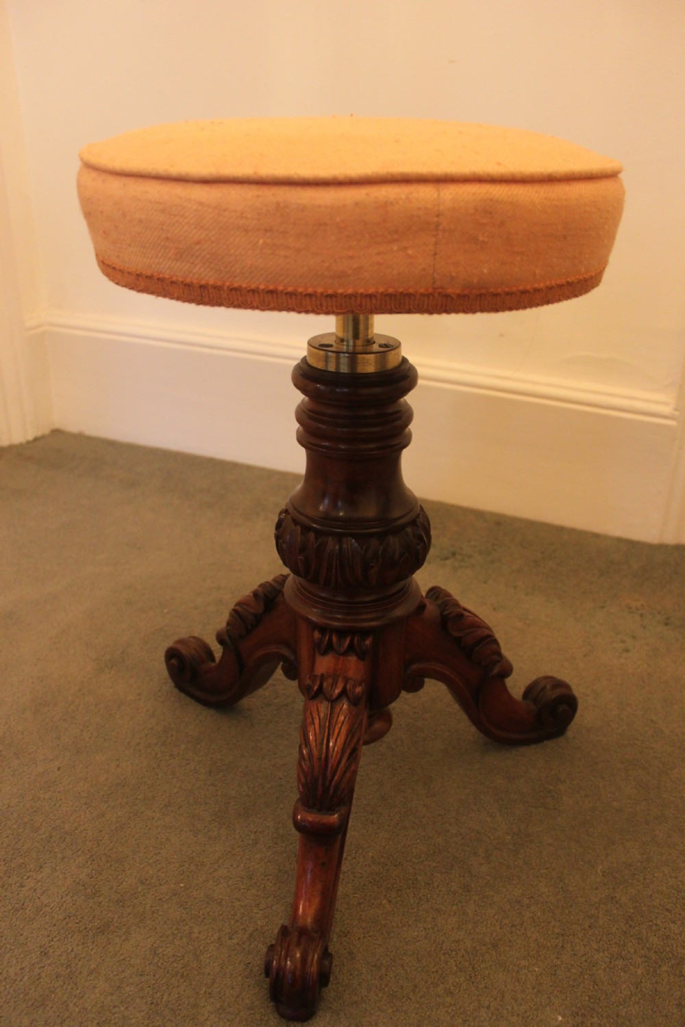 A Victorian mahogany revolving piano stool featuring a circular beige upholstered seat, a turned pedestal with acanthus leaf carving, and tripod scroll feet. View VII