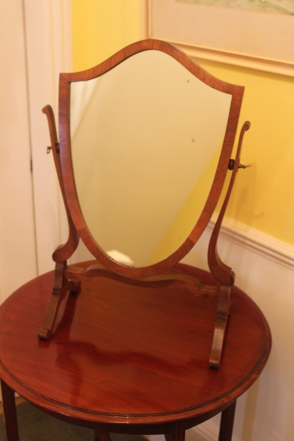 An Edwardian Hepplewhite style mahogany toilet mirror featuring a shield-shaped frame supported by two curved upright legs.
