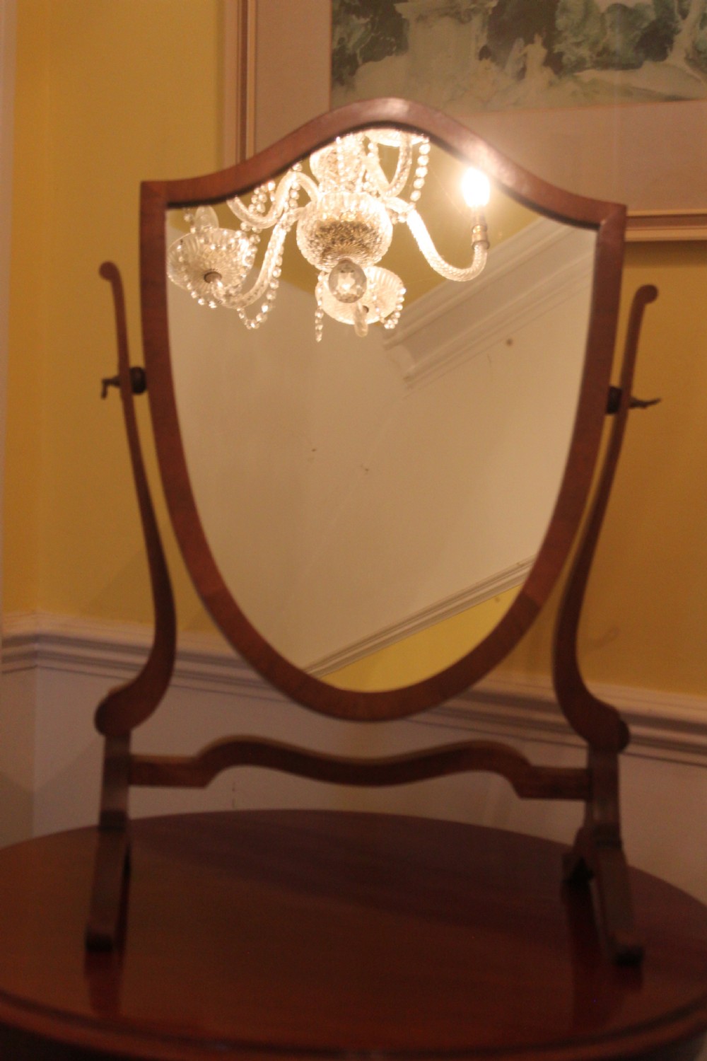 An Edwardian Hepplewhite style mahogany toilet mirror featuring a shield-shaped frame supported by two curved upright legs. View II