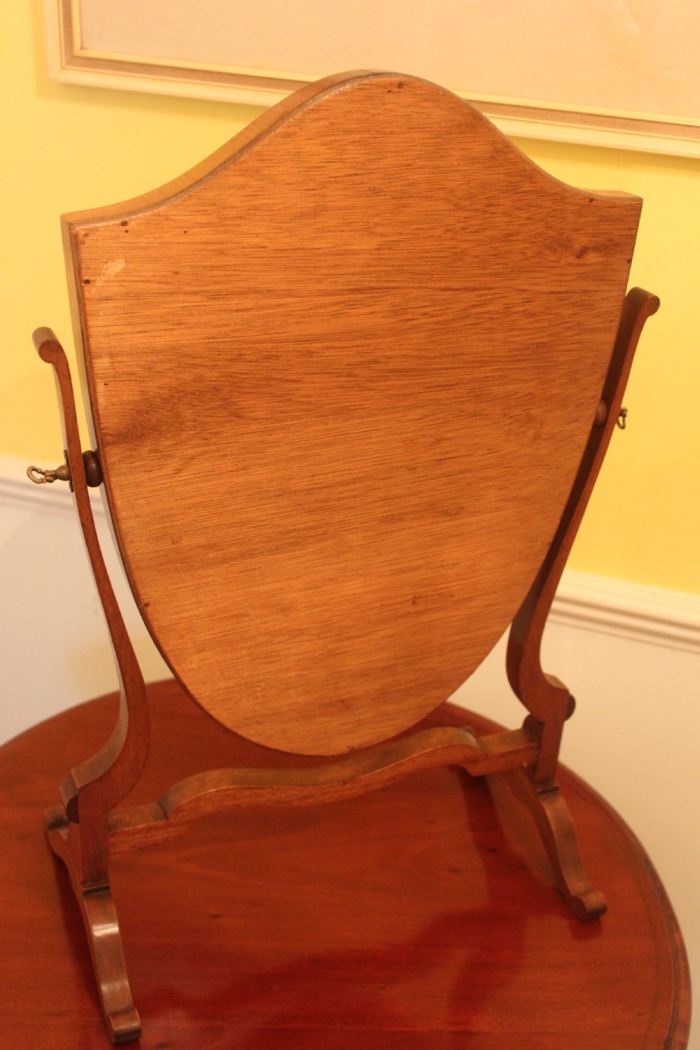An Edwardian Hepplewhite style mahogany toilet mirror featuring a shield-shaped frame supported by two curved upright legs. View VI