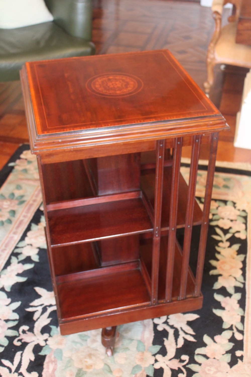 An Edwardian mahogany revolving bookcase featuring a central satinwood marquetry inlay top, slatted sides, open shelves, and castors.