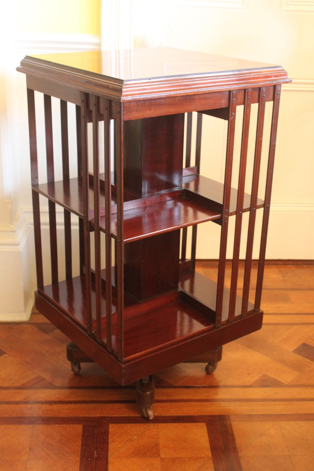 An Edwardian mahogany revolving bookcase featuring a central satinwood marquetry inlay top, slatted sides, open shelves, and castors. View III