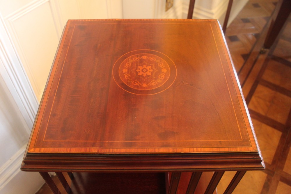 An Edwardian mahogany revolving bookcase featuring a central satinwood marquetry inlay top, slatted sides, open shelves, and castors. View V