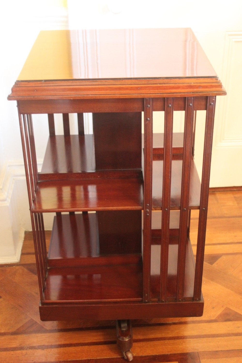 An Edwardian mahogany revolving bookcase featuring a central satinwood marquetry inlay top, slatted sides, open shelves, and castors. View VIII