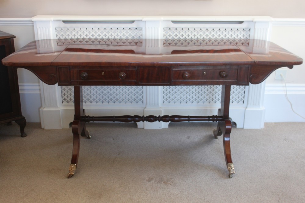 An early nineteenth-century mahogany sofa table featuring two drop leaves, two frieze drawers with knob handles, a turned central stretcher, and splayed legs with brass paw feet and castors. View II