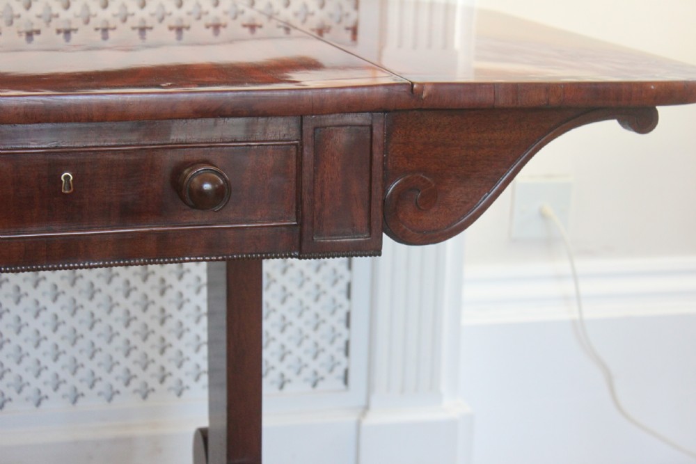 An early nineteenth-century mahogany sofa table featuring two drop leaves, two frieze drawers with knob handles, a turned central stretcher, and splayed legs with brass paw feet and castors. View III