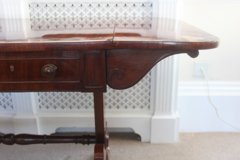 An early nineteenth-century mahogany sofa table featuring two drop leaves, two frieze drawers with knob handles, a turned central stretcher, and splayed legs with brass paw feet and castors. View VI