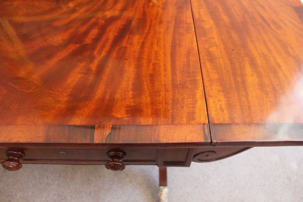 An early nineteenth-century mahogany sofa table featuring two drop leaves, two frieze drawers with knob handles, a turned central stretcher, and splayed legs with brass paw feet and castors. View VIII