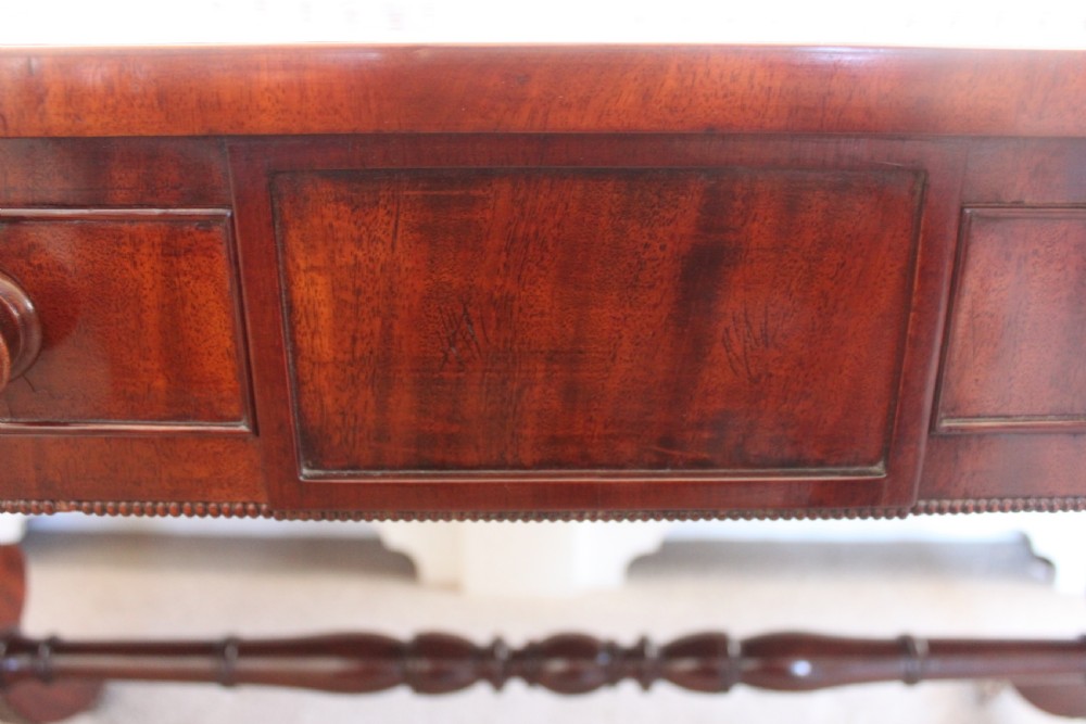 An early nineteenth-century mahogany sofa table featuring two drop leaves, two frieze drawers with knob handles, a turned central stretcher, and splayed legs with brass paw feet and castors. View XII